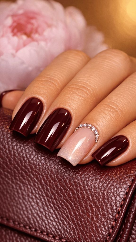 Burgundy square nails with one sheer shimmer accent nail adorned with a crystal half-moon detail