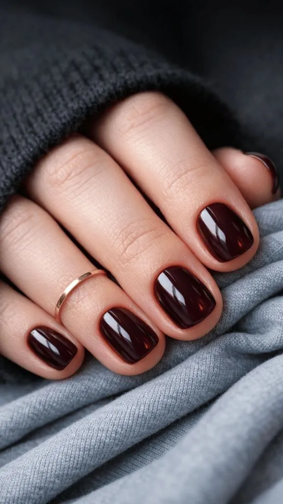 Short natural nails in a deep, glossy burgundy-brown shade