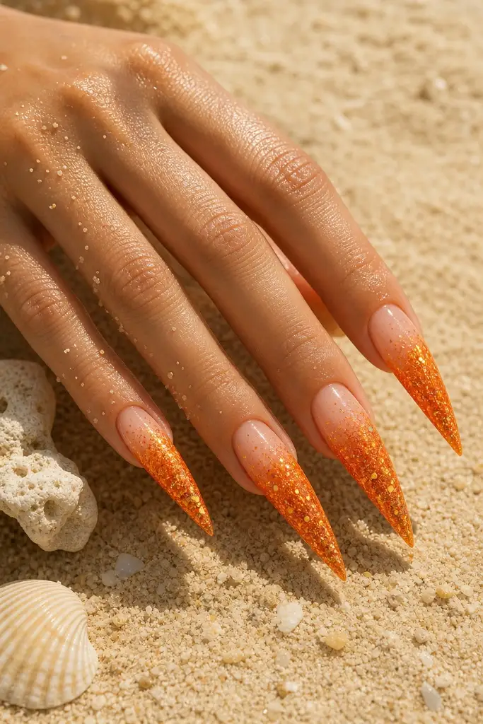 Sunset Glitter Stiletto nails for summer. Summer vibes nails 2026 in orange glitter ombre on long claws.