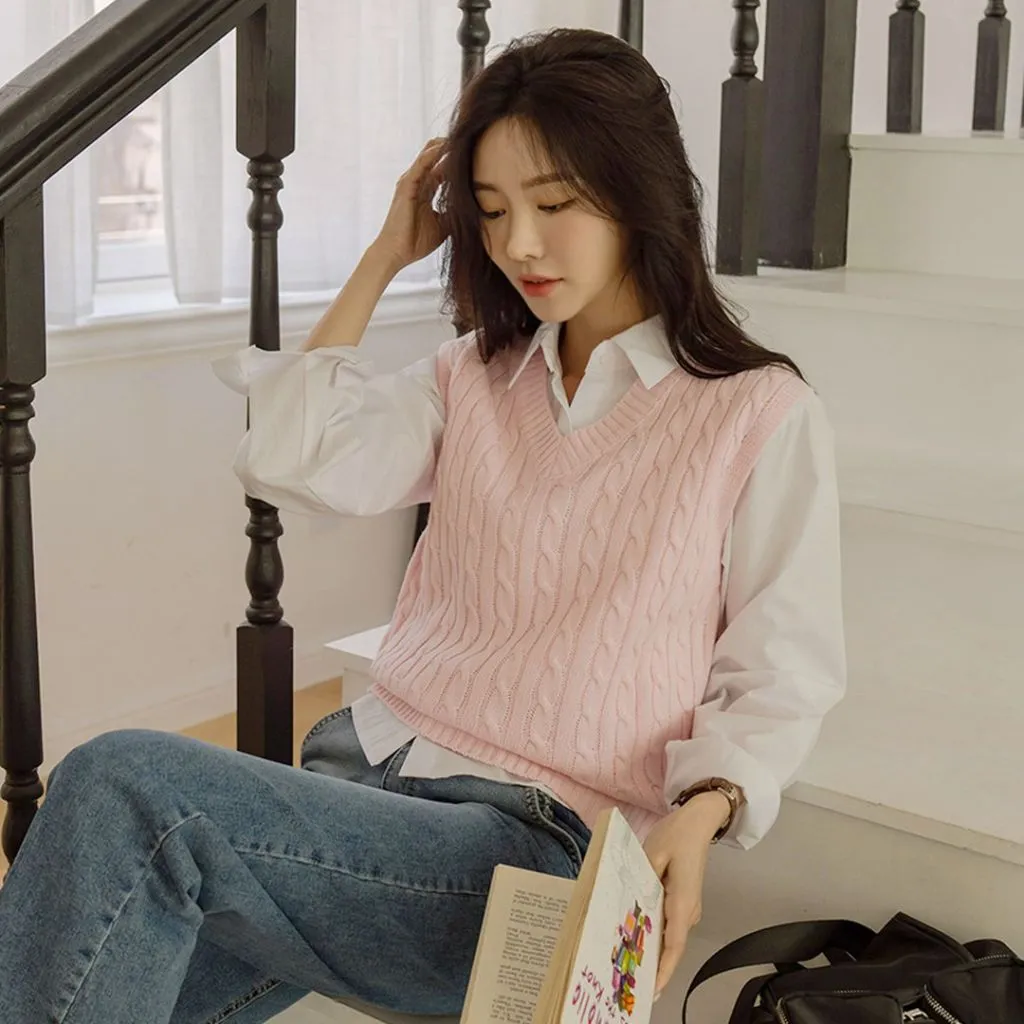 Pink cable knit V-neck sweater vest layered over white button-down shirt with blue jeans