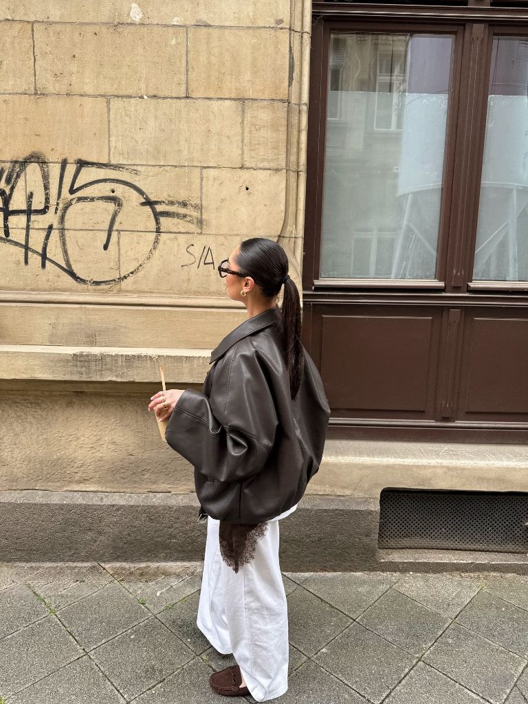 Brown leather oversized jacket from behind with white skirt and moccasins