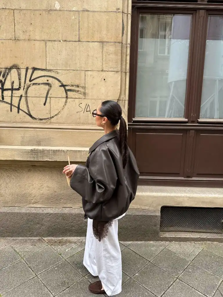 Brown leather oversized jacket from behind with white skirt and moccasins