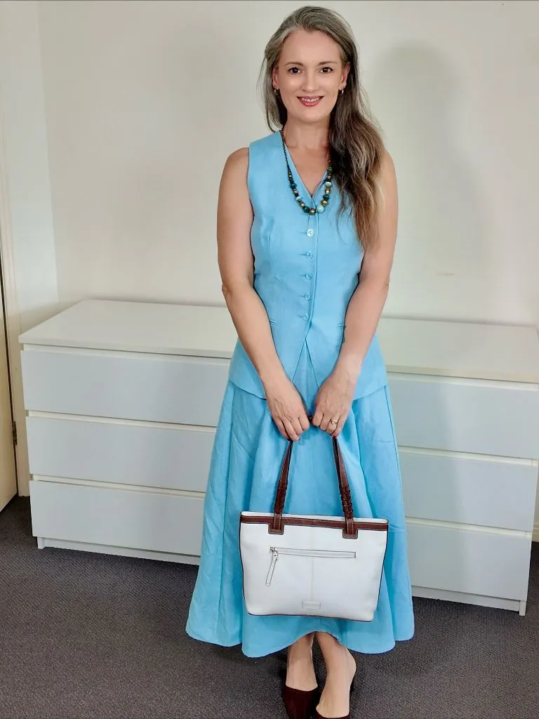 Light blue sleeveless linen dress with beaded necklace and white bag