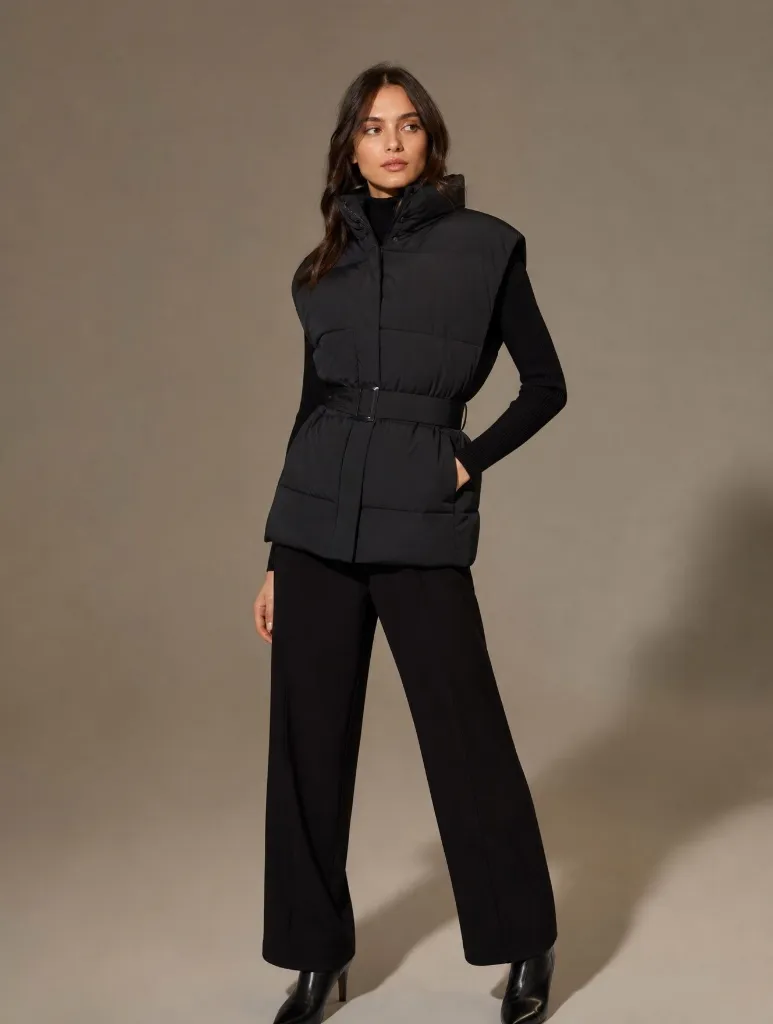 Black belted puffer vest over knit top with black trousers