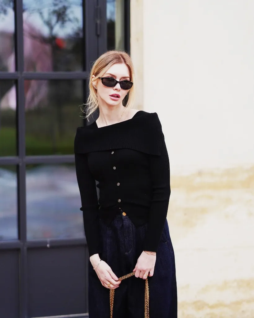 Black off-shoulder button-front knit with dark jeans and gold chain bag