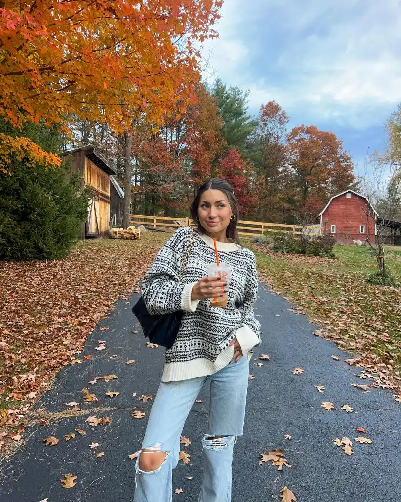 Fair Isle sweater with ripped light-wash jeans in autumn foliage setting