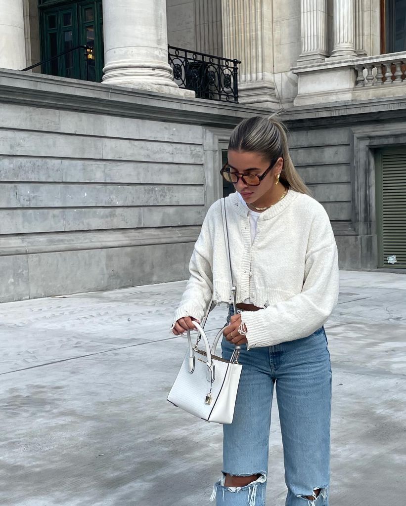 White cropped cardigan with ripped jeans and white mini bag in city setting