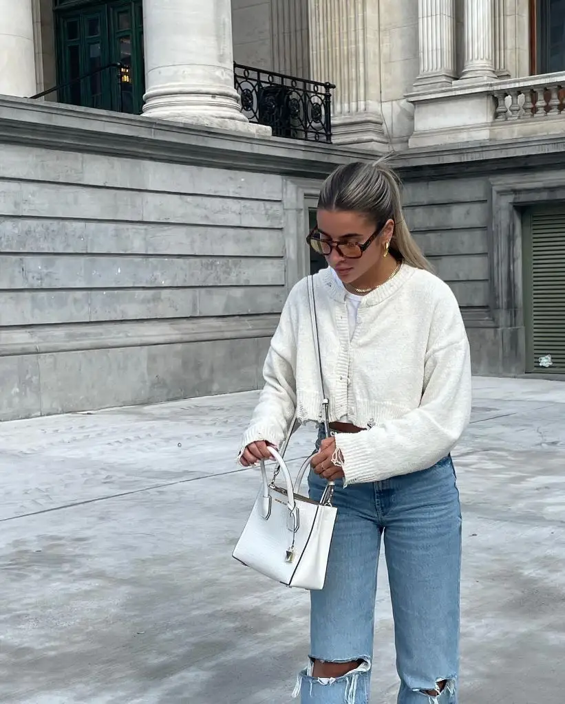 White cropped cardigan with ripped jeans and white mini bag in city setting