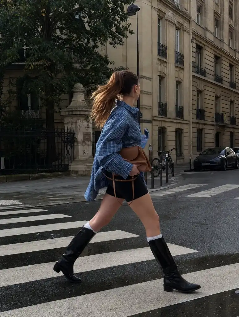 Woman crossing a Paris crosswalk in oversized blue checked shirt, bike shorts, socks and tall black boots
