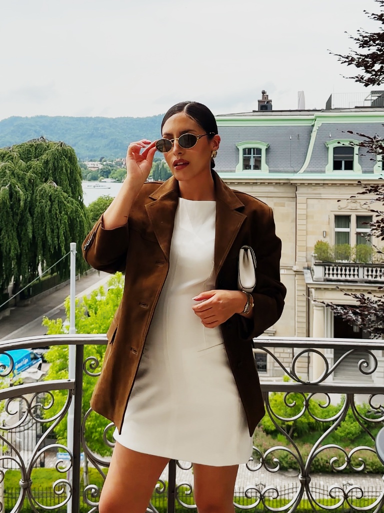 White mini dress with brown suede blazer on a balcony overlooking Zurich