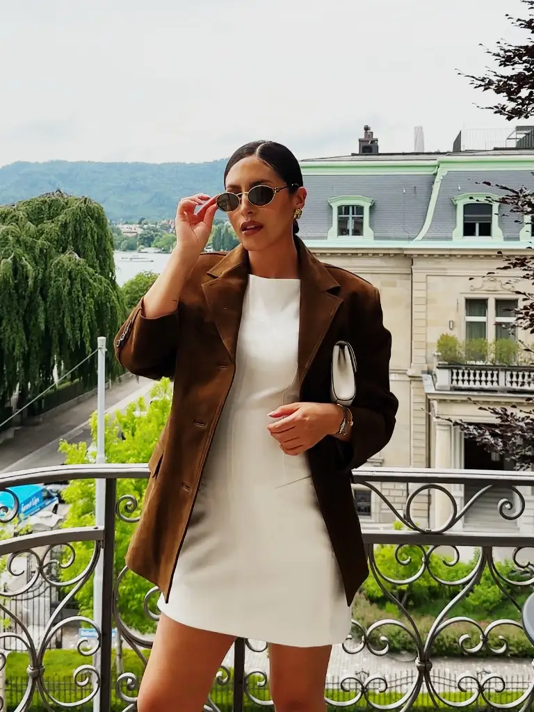 White mini dress with brown suede blazer on a balcony overlooking Zurich