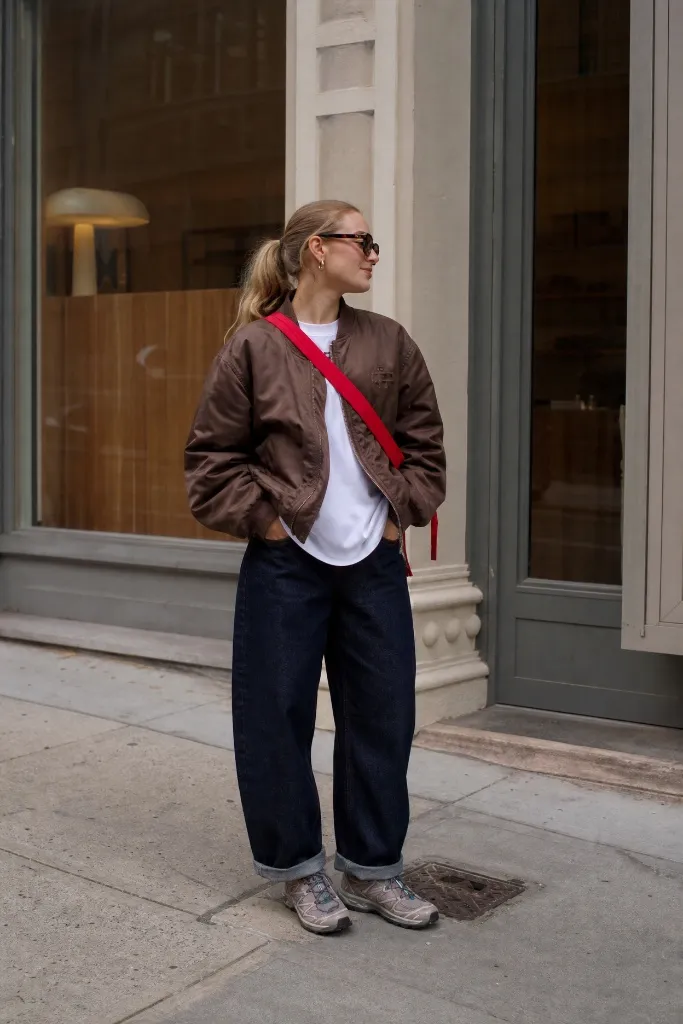 Brown bomber jacket with white tee, dark wide jeans and gray sneakers