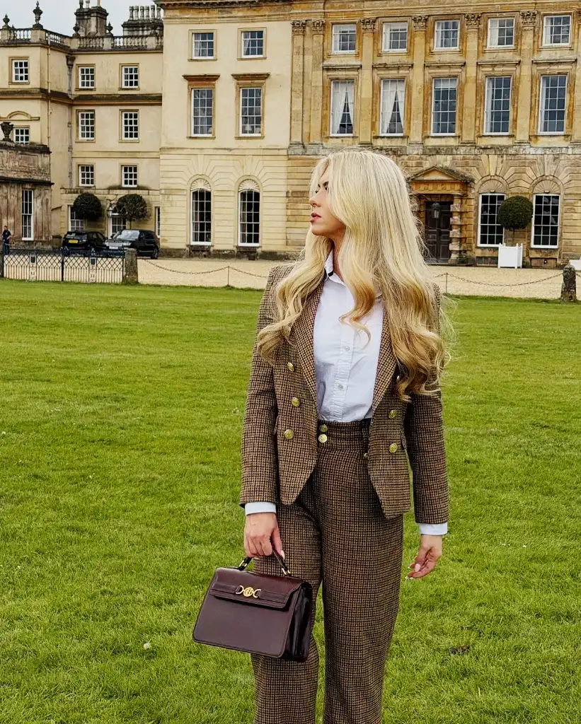 Brown houndstooth suit with white shirt and burgundy structured bag at a country estate