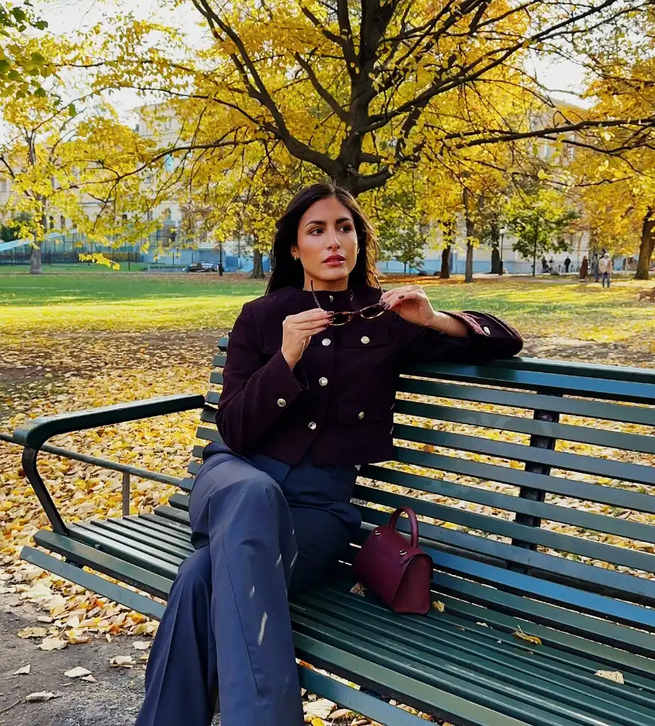 Burgundy military-style jacket with navy wide-leg trousers on a park bench with fall foliage