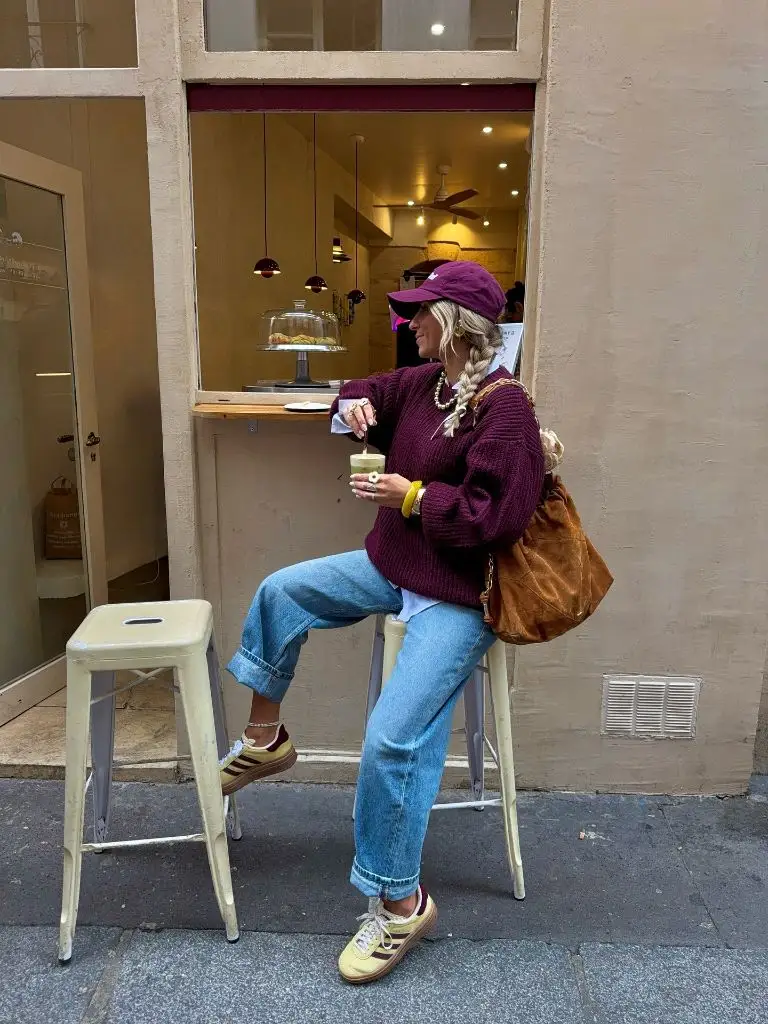Burgundy sweater, jeans, and retro Adidas sneakers at a Paris café