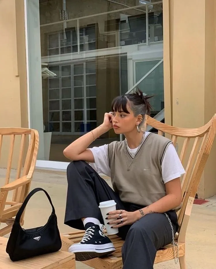 Taupe Nike sweater vest over white t-shirt with dark wide-leg trousers, Prada nylon bag, and Converse platform sneakers