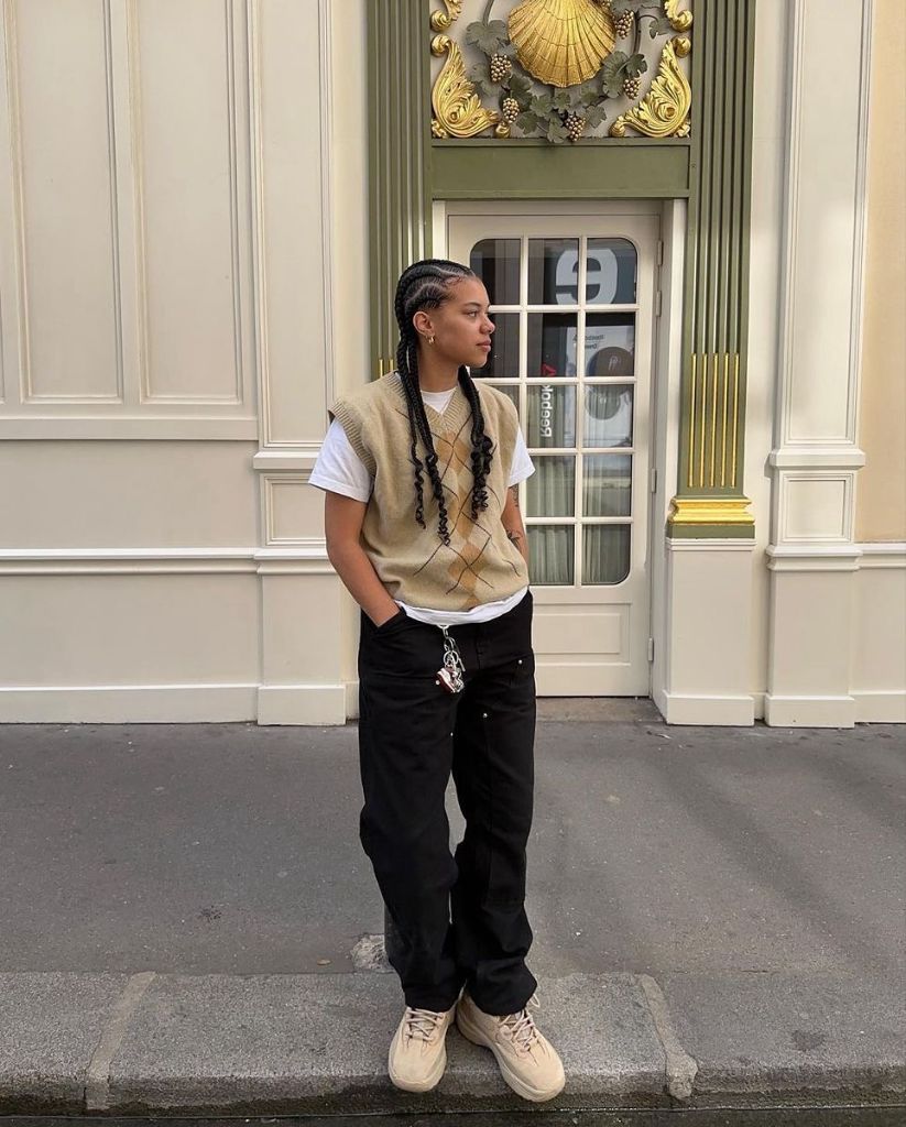 Beige argyle sweater vest over white t-shirt with black cargo pants, beige sneakers, and chain accessories