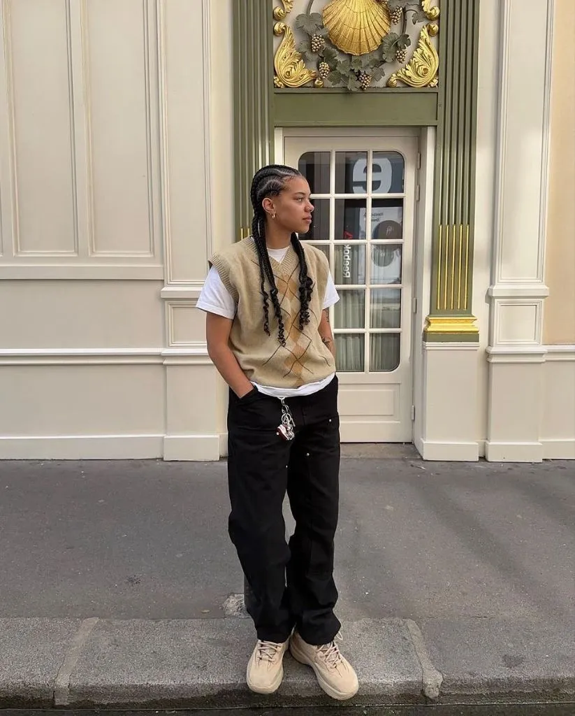 Beige argyle sweater vest over white t-shirt with black cargo pants, beige sneakers, and chain accessories