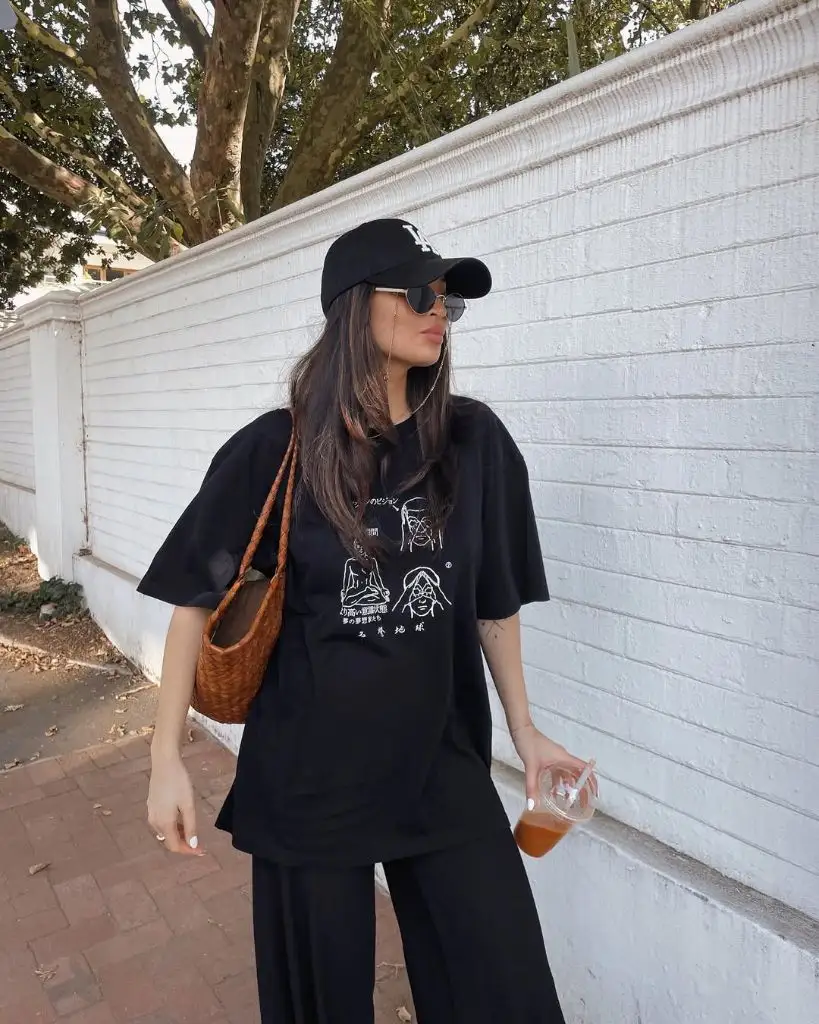 All-black outfit with Japanese graphic oversized tee, wide-leg pants, black cap, woven brown bag