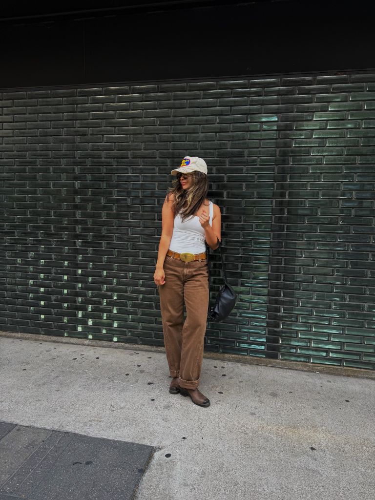 White tank top with brown pants, belt, and cap