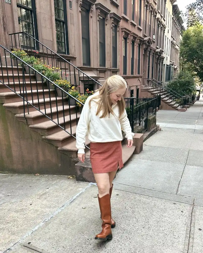 Cream quarter-zip pullover with red mini skirt and riding boots