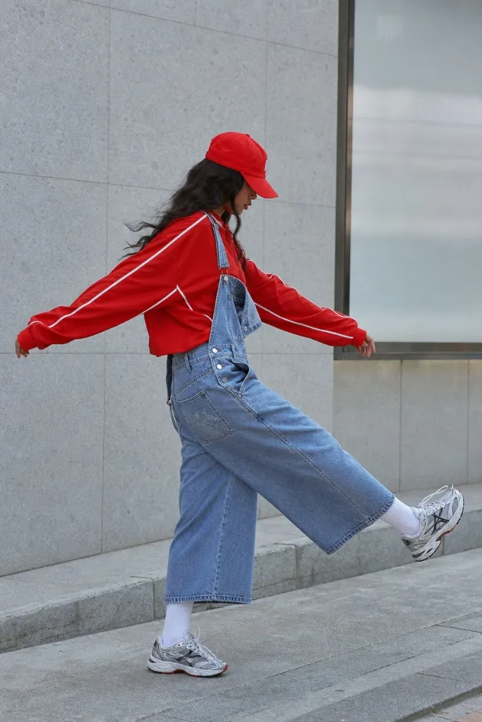 Red track jacket with denim overalls and sneakers