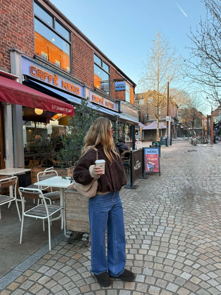 Brown bomber jacket with wide-leg jeans and platform boots outside Caffè Nero