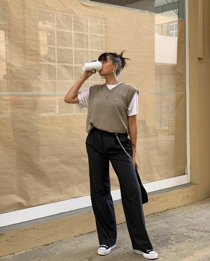 Taupe Nike V-neck sweater vest over white tee with black wide-leg trousers, Converse sneakers, chain crossbody bag, and layered necklaces