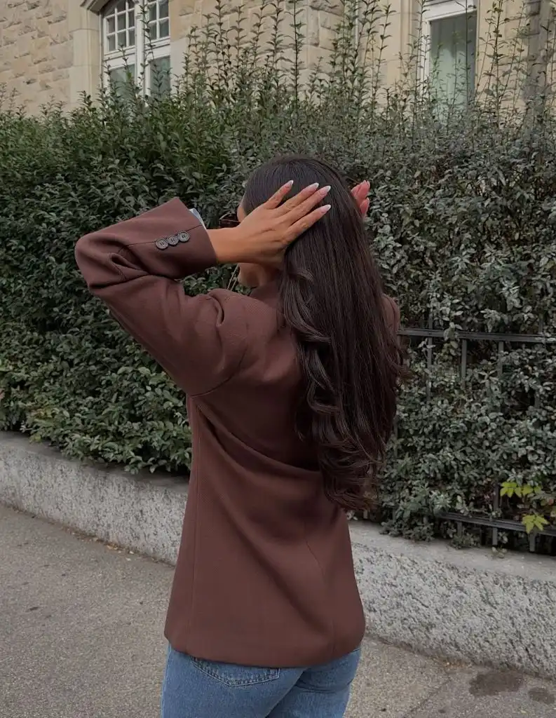 Chocolate brown oversized blazer from behind with dark wavy hair and blue jeans on a leafy European street
