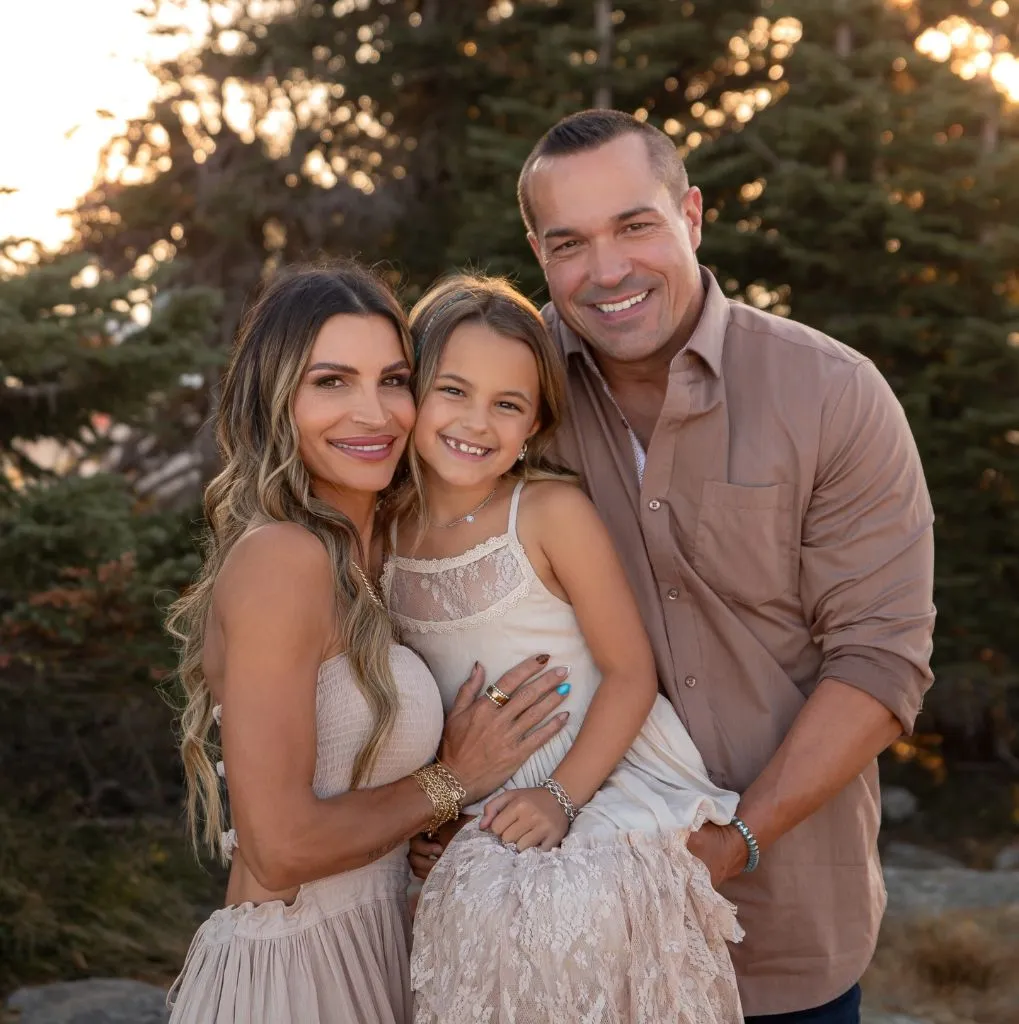 Family of three with parents and daughter in neutral blush and taupe tones at sunset