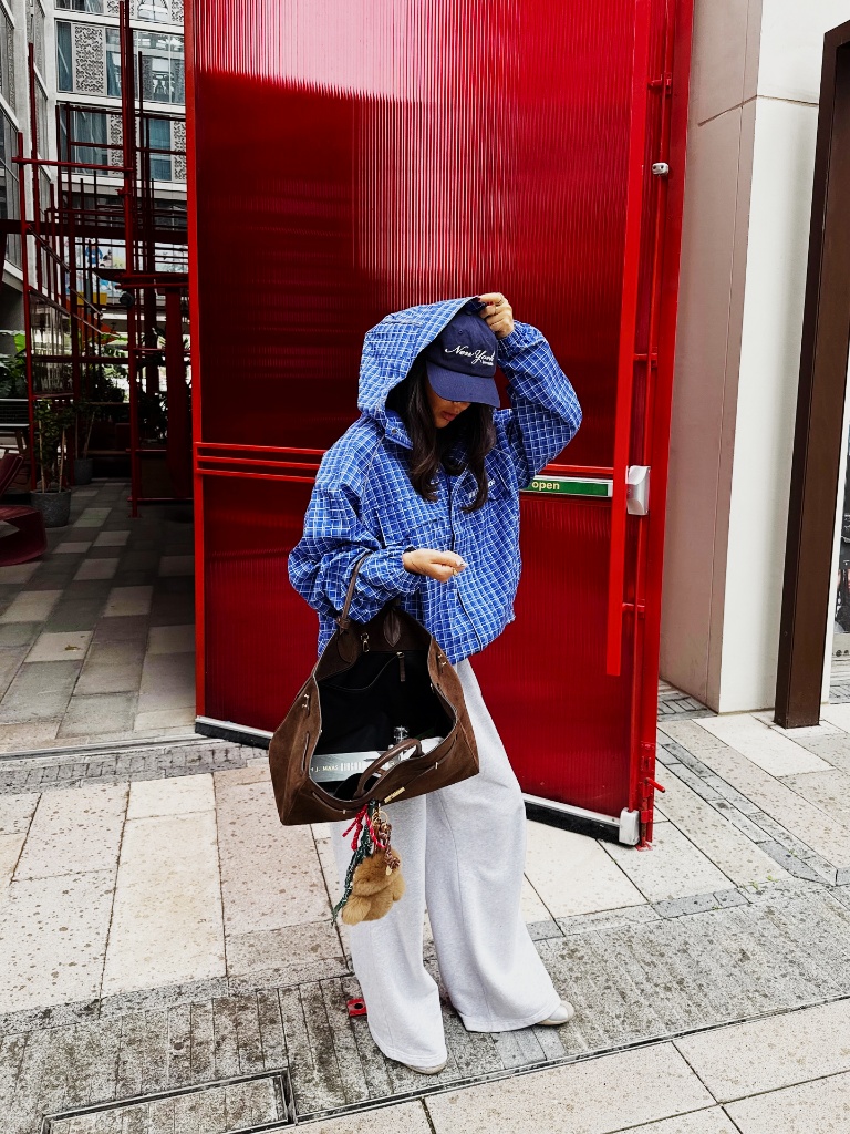 Blue check anorak with grey sweatpants, baseball cap, and brown suede tote