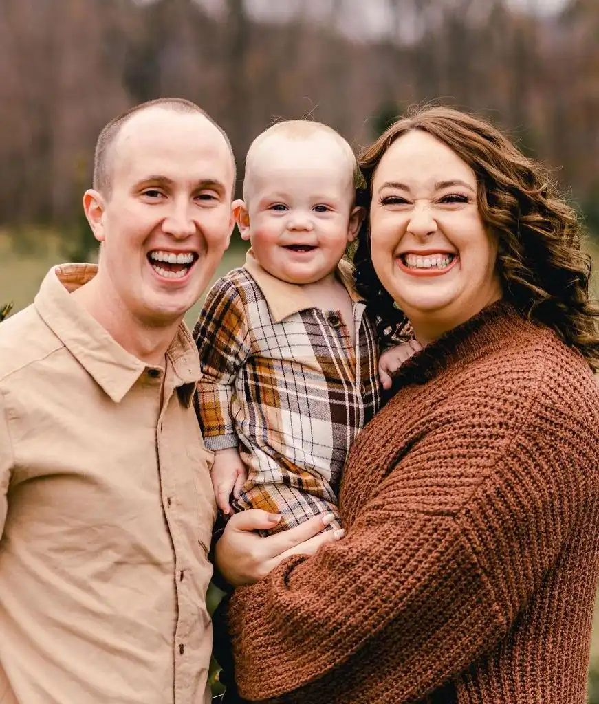 Close-up family photo of parents and baby in warm rust and plaid tones