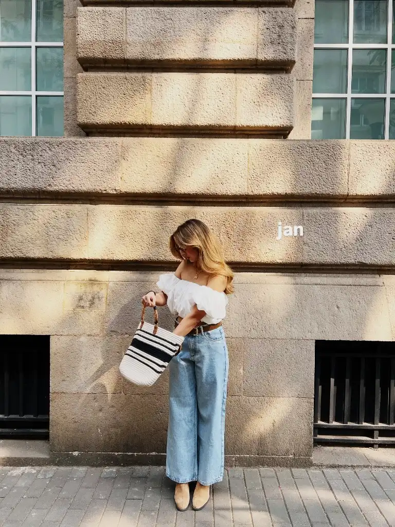 White off-shoulder puff-sleeve top with light wash wide-leg jeans and straw bag