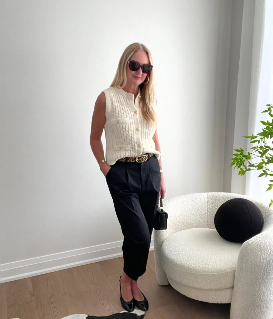 Cream cable knit button-front vest with leopard print belt, navy trousers, black pointed flats, and small black handbag