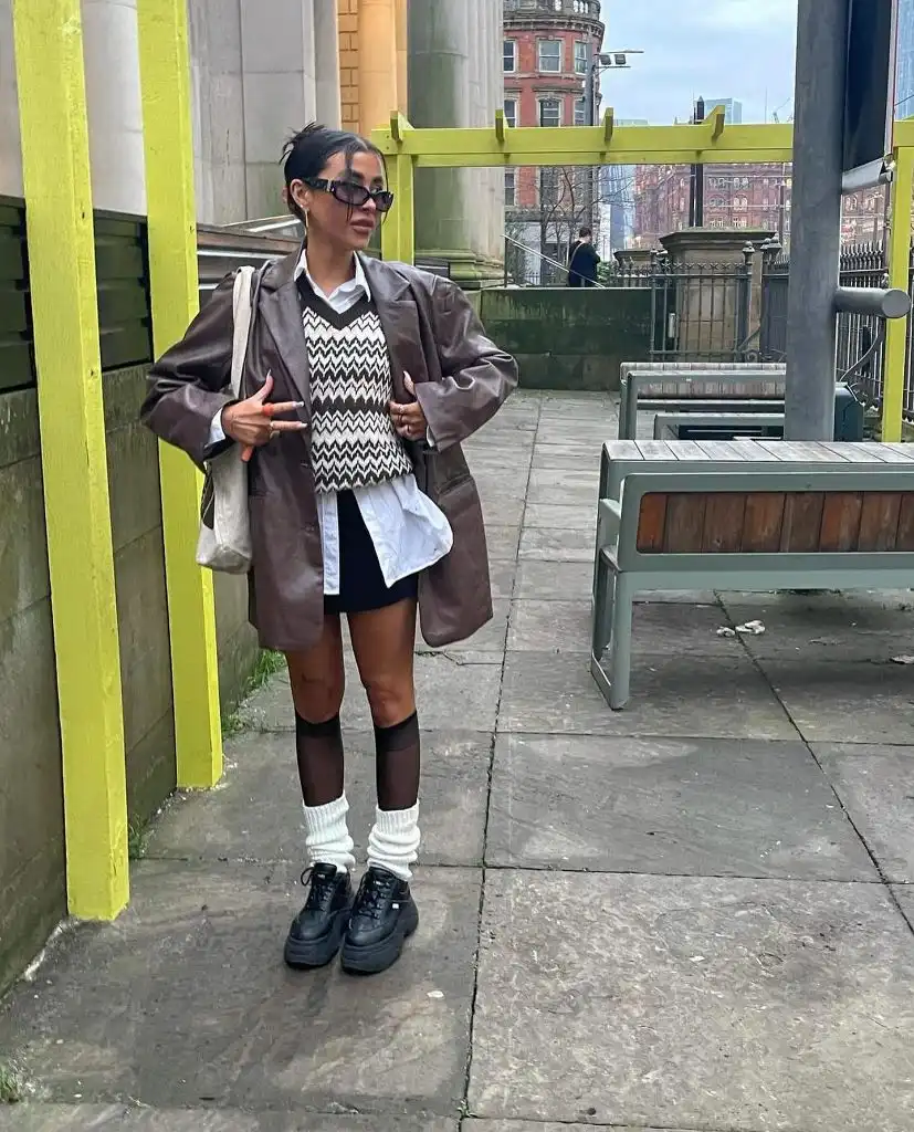 Black and white zigzag pattern sweater vest under brown oversized leather blazer with mini skirt, sheer knee-high stockings, chunky white socks, and platform sneakers