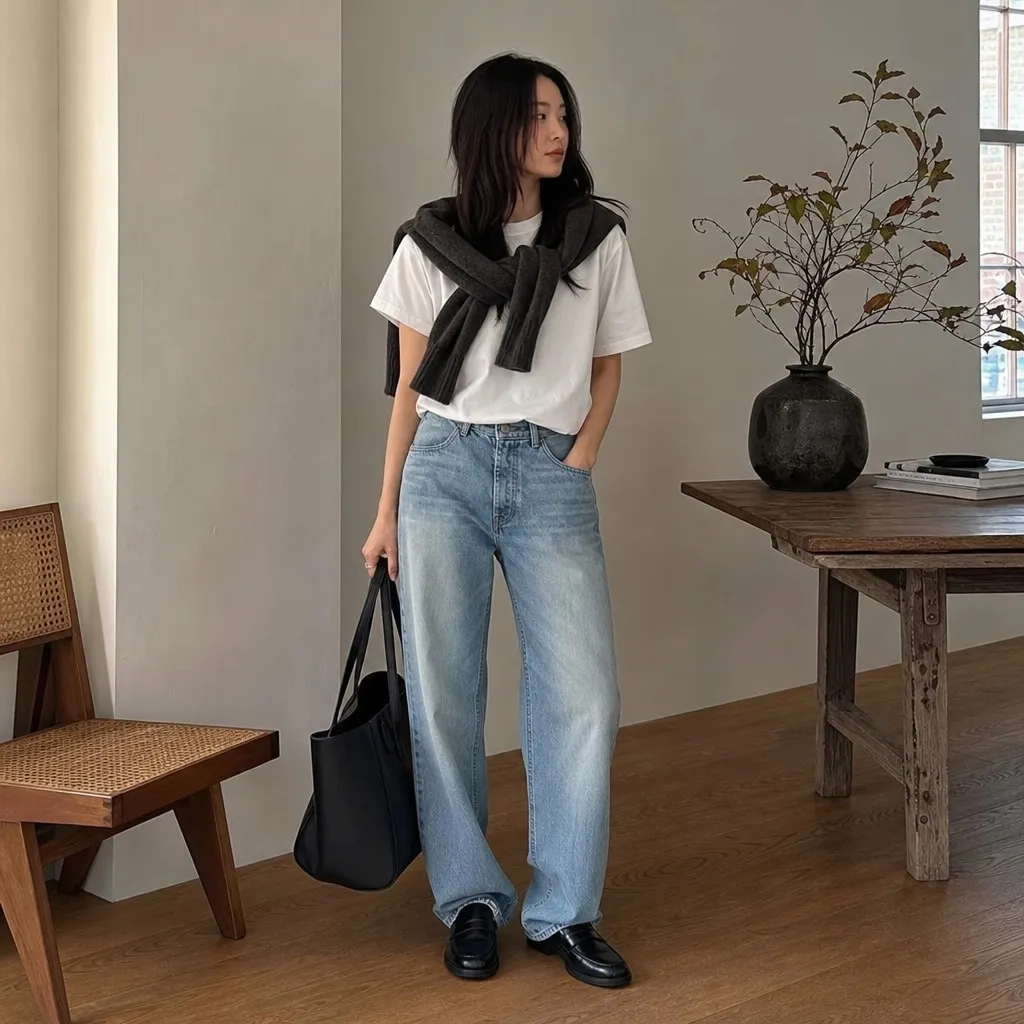 White tee with dark sweater draped over shoulders and wide-leg jeans