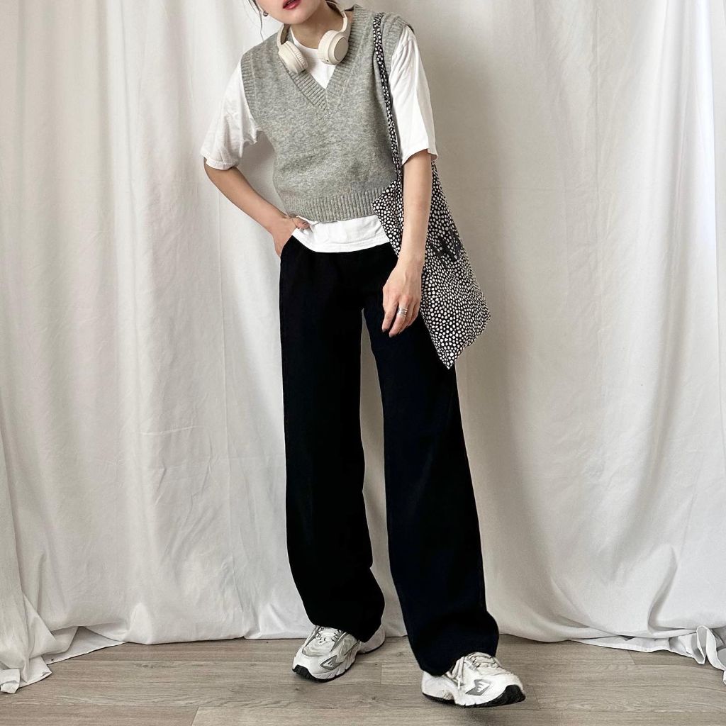 Grey V-neck cropped sweater vest over white t-shirt with black wide-leg trousers, New Balance sneakers, polka-dot tote, and headphones