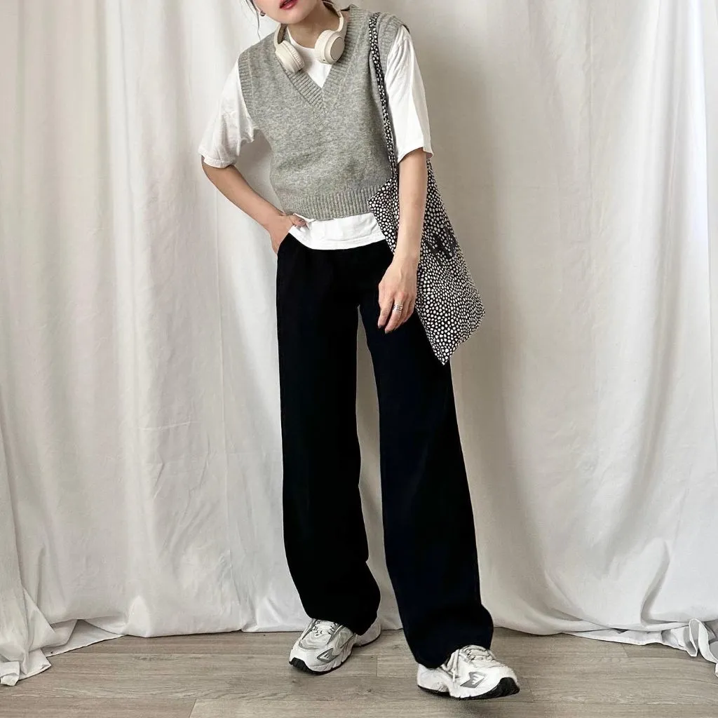 Grey V-neck cropped sweater vest over white t-shirt with black wide-leg trousers, New Balance sneakers, polka-dot tote, and headphones