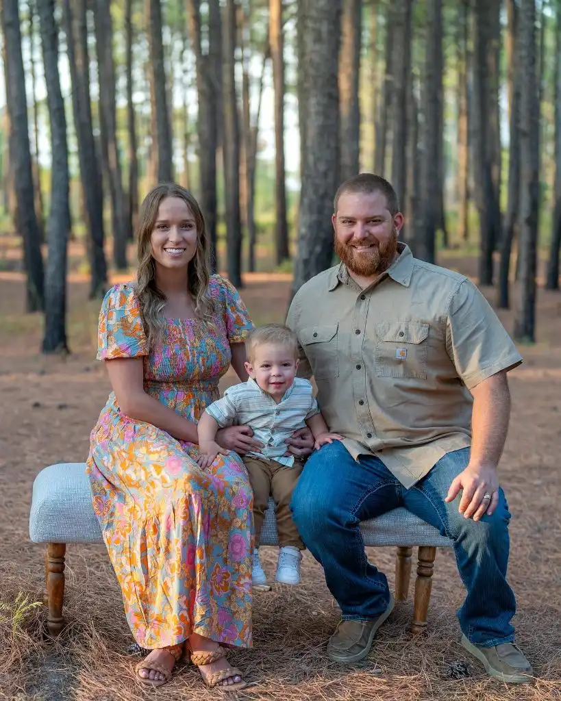 Family of three seated on bench in pine forest with colorful floral dress and Carhartt shirt