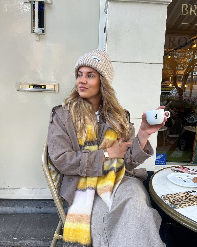 Beige Ganni beanie with taupe coat and yellow plaid scarf at a café
