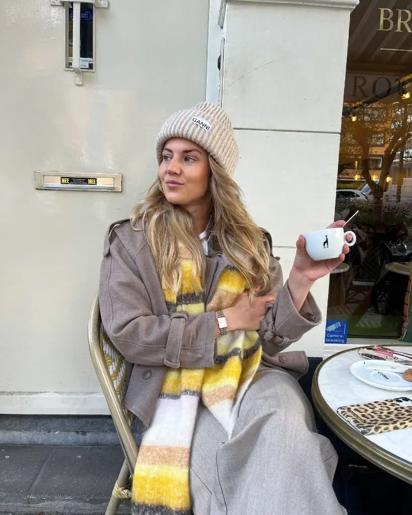 Beige Ganni beanie with taupe coat and yellow plaid scarf at a café