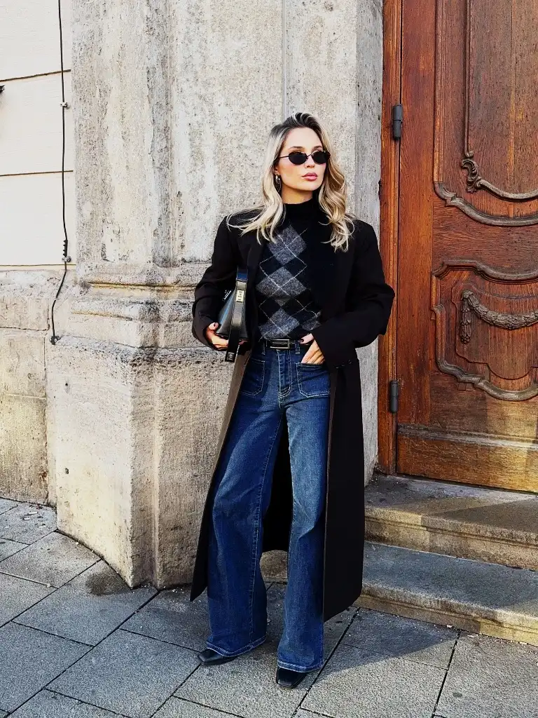 Black argyle sweater with long black coat, wide-leg jeans, and black bag