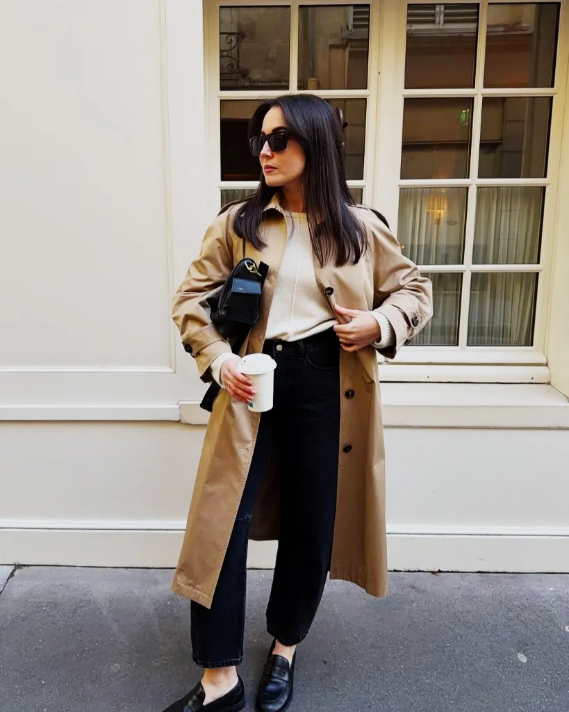Tan trench coat with black jeans, cream sweater, and loafers in Paris