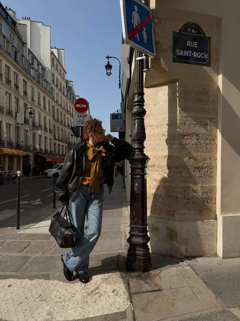 Black leather jacket with mustard scarf, blue jeans and loafers in Paris