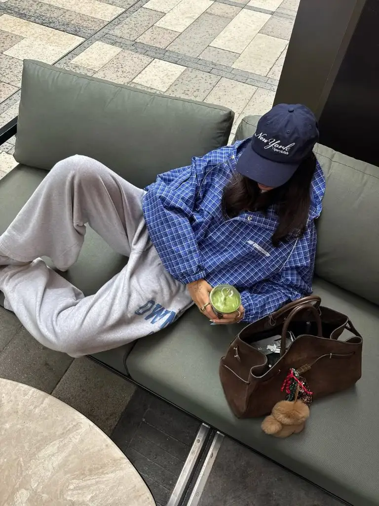 Blue check oversized shirt with grey logo sweatpants, navy New York cap, brown suede bag, matcha latte
