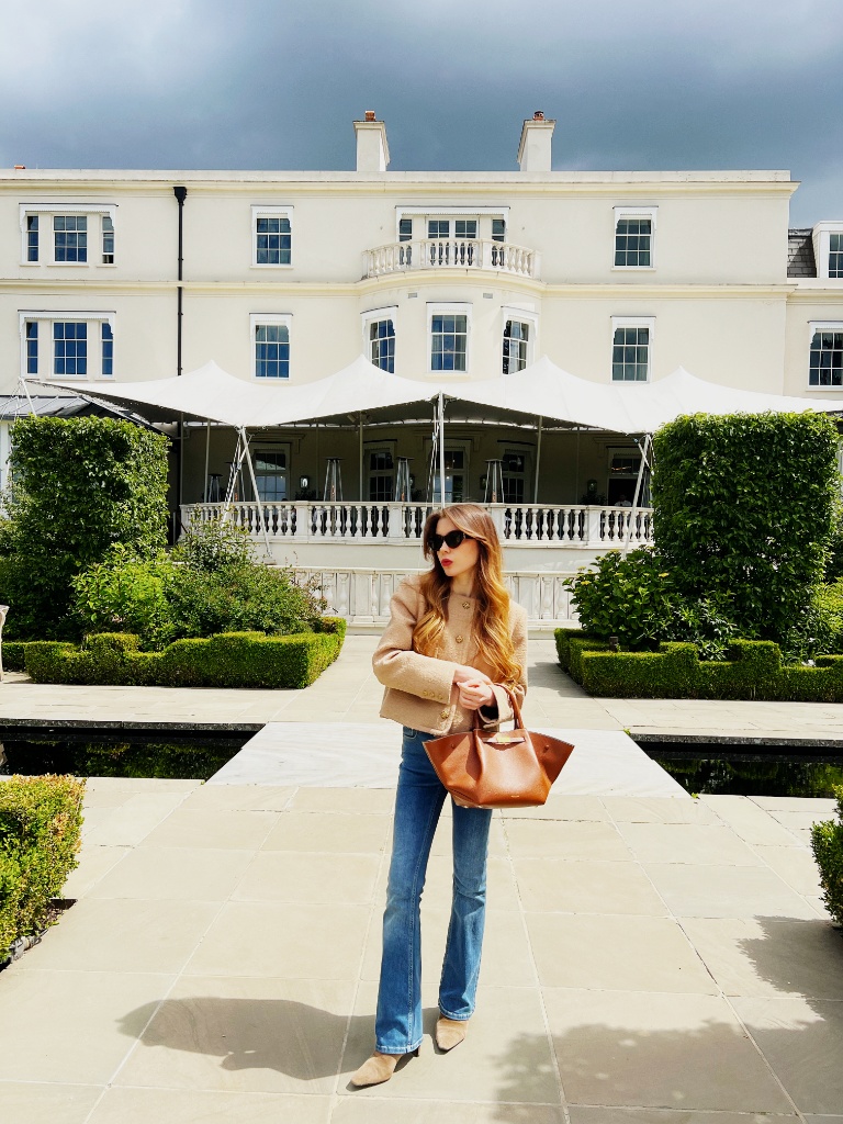 Camel tweed blazer with flared jeans and cognac leather tote at a country estate