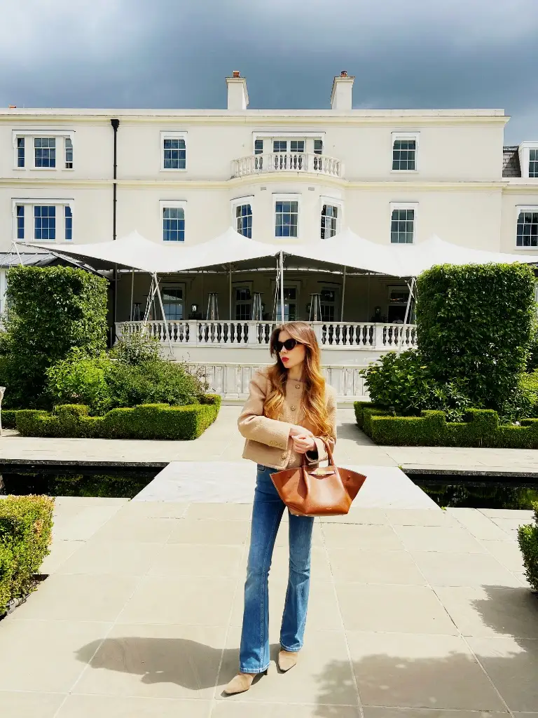 Camel tweed blazer with flared jeans and cognac leather tote at a country estate