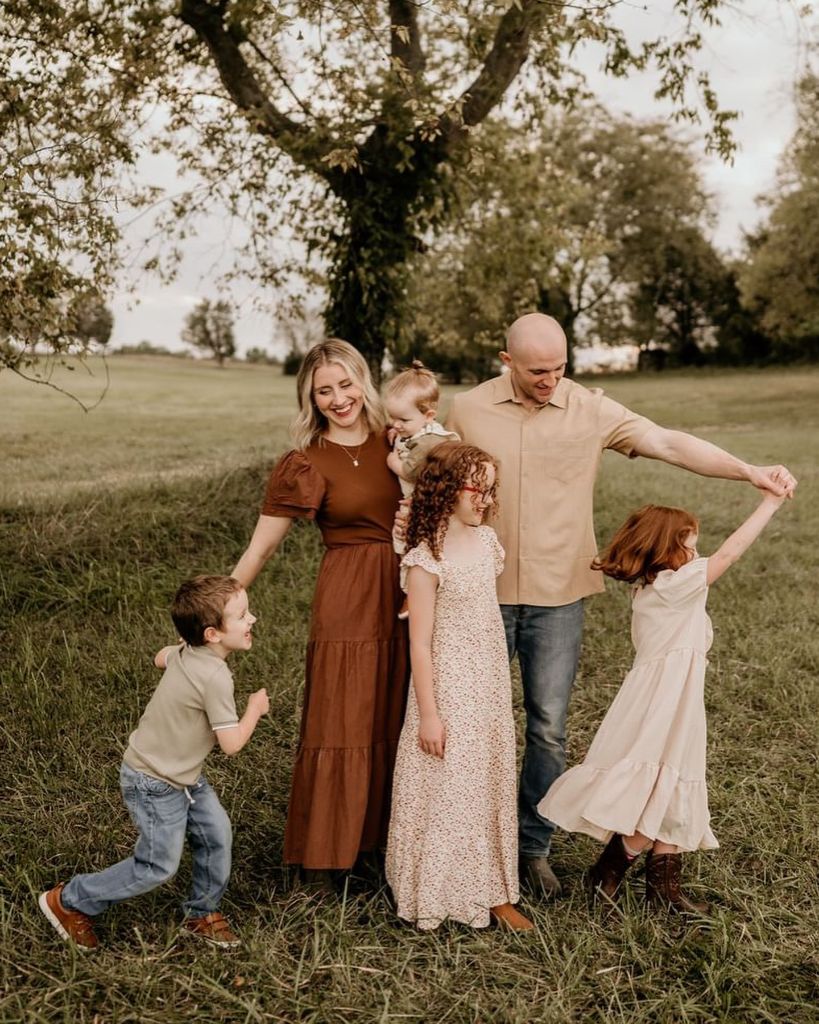 Family of six in earthy tones playing in a green field under a tree