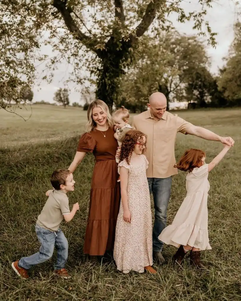 Family of six in earthy tones playing in a green field under a tree
