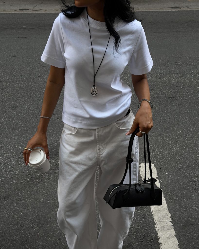All-white outfit with white t-shirt, white wide-leg jeans, pendant necklace and small black bag